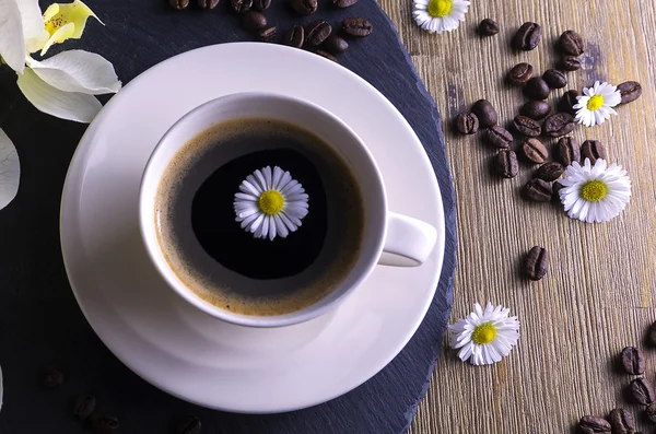 Siyah çay siyah ve kahverengi bir arka plan ile yapılan kompozisyon. Beyaz çiçek, papatya ve kahve çekirdekleri ile siyah kahve fincan. Bu simbolizes güzel sabah lezzetli çay ile.