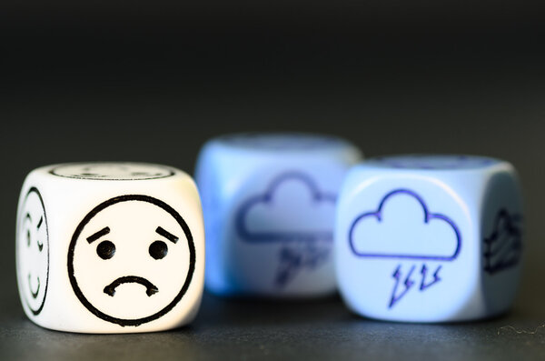 concept of sad storm weather - emoticon and weather dice on blac