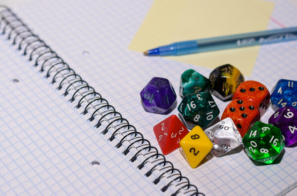 open exercise book with sticky card, pen and role playing dices