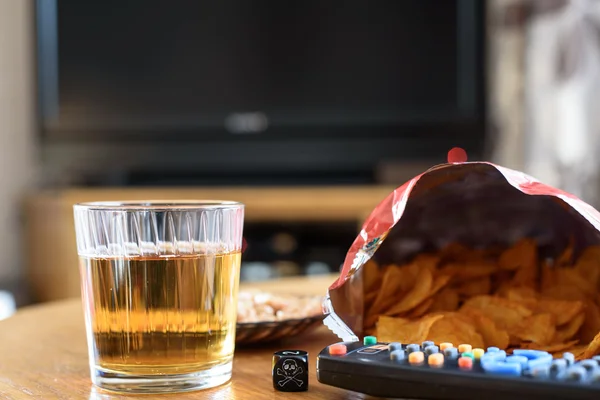 Ungesundes Essen auf dem Tisch mit Totenkopfwürfeln und Fernseher im Hintergrund — Stockfoto