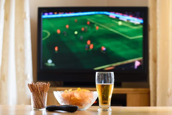 TV, TV-tittande (fotboll, fotbollsmatch) med snacks ligg Stockbild