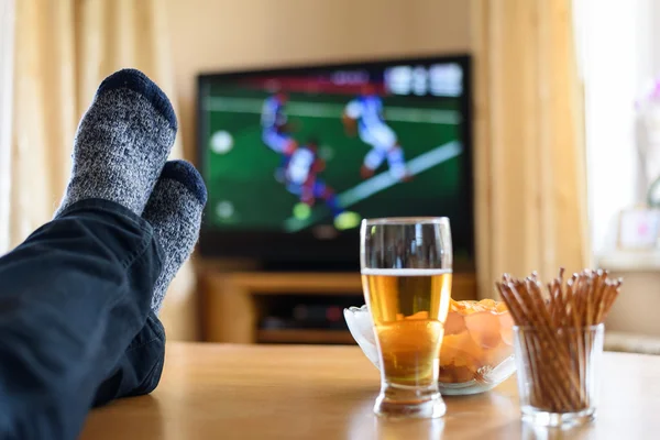 TV, TV-tittande (fotbollsmatch) med fötterna på bordet och Royaltyfria Stockfoton