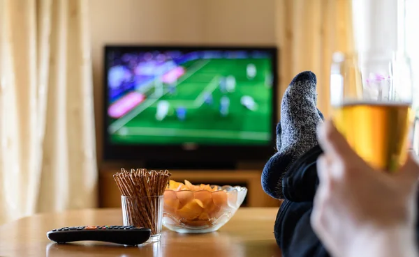 TV, TV-tittande (fotbollsmatch) med fötterna på bordet och Stockbild