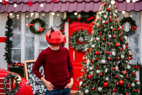 A young man in a bull ox costume is a symbol of the new year against the background of a red car, a festive Christmas tree, decorated with garlands of porch lights with a wreath. Copy space, template