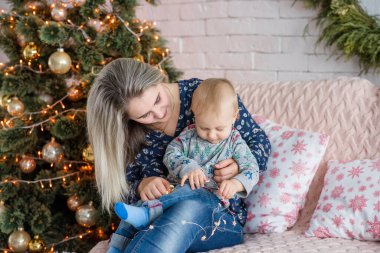 Güzel genç bir kadın, Noel ağacının yanında beyaz bir duvara yaslanmış bir çocukla bir kanepede oturuyor. Anne kucaklar, öper, küçük oğluyla oynar. Mutlu aile yeni yılı kutlar. Boşluğu kopyala, şenlikli 