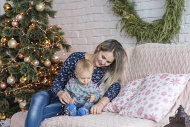 Güzel genç bir kadın, Noel ağacının yanında beyaz bir duvara yaslanmış bir çocukla bir kanepede oturuyor. Anne kucaklar, öper, küçük oğluyla oynar. Mutlu aile yeni yılı kutlar. Boşluğu kopyala, şenlikli 