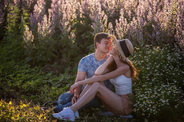 恋爱中的一对幸福的夫妻坐在一片盛开的圣园旁拥抱 一个年轻人热情地拥抱 牵着手 看着戴着草帽的漂亮姑娘的眼睛 情侣周末旅行 复制空间 — 图库照片