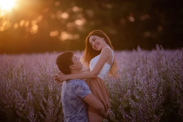 年轻的男人抱着美丽的女人 在夕阳西下的光芒中 旋转着她绕着盛开的紫罗兰花园地 这个女孩的头发向不同的方向飘扬着 一个结婚的提议 复制空间 — 图库照片