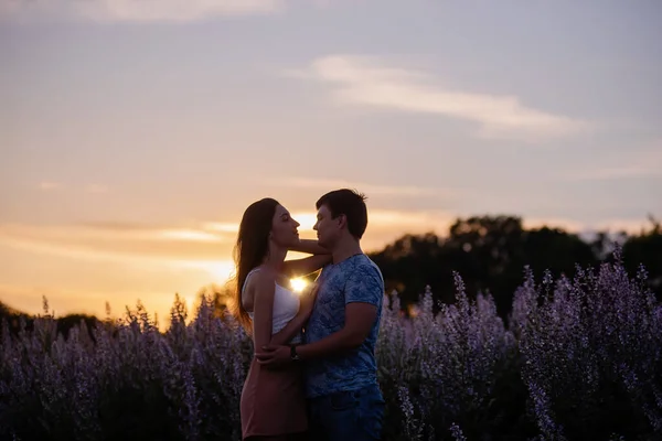 愛の抱擁で幸せなカップルは 開花期のフィールドの近くの日没でキス 若い男が熱心に目を覗き込み 美しい少女を手で抱いている 恋人春の週末旅行 スペースのコピー — ストック写真