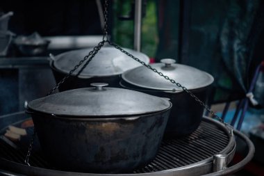 Izgaranın üzerinde büyük gri alüminyum kazanlar var. Bu kazanda bir kamp ateşi, hafta sonu ormanda yapılacak bir festivale hazırlanıyor..