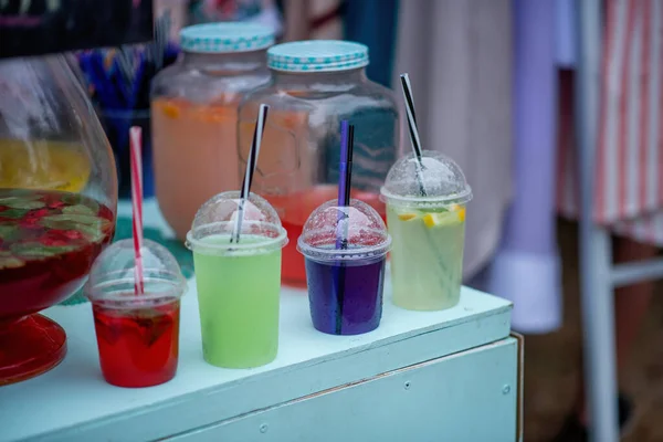 At a street food festival, colorful cocktails are displayed on the counter in disposable glasses with straws, smoking from artificial ice inside. Wine sangria, homemade lemonades.