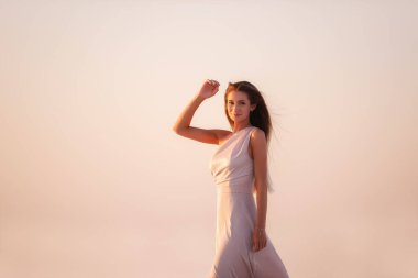 Akşam havası pembeli, tozlu bir elbise içindeki genç sarışın bir kadının portresi güzel bir günbatımının arka planında. Doğal makyajlı bir kız, havada saçlar uzuyor. Boşluğu kopyala