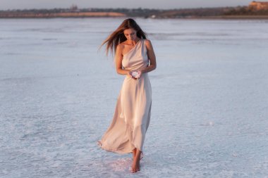 Akşamları havadar, pastel, pembe pudralı elbisesi olan genç sarışın kadın elinde kristalize olmuş beyaz tuz parçaları tutuyor. Doğal makyajlı bir kız, saçı gelişiyor. Tuz madenciliği gezisi, gün batımında suda yürümek.