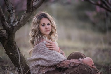 Genç, kıvırcık saçlı, kahverengi pileli etekli, pembe bluzlu, omuzları örülü atkıyla kaplı, günbatımı bahçelerinde oturan güzel bir kadın. Kız şehrin dışında yürümekten zevk alıyor, doğal güzellik.