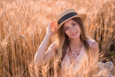 Buğday ve çavdar dikenli altın bir tarlada hasır şapkalı genç sarışın kadın. Kahverengi gözlü güzel bir kızın yakın plan portresi. Hafta sonu şehir dışında yürüyüş. Tarım dokusu