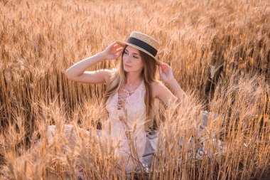 Buğday ve çavdar dikenli altın bir tarlada hasır şapkalı genç sarışın kadın. Kahverengi gözlü güzel bir kızın yakın plan portresi. Hafta sonu şehir dışında yürüyüş. Tarım dokusu