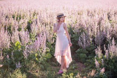Pembe adaçayının çiçek açmış arka planında açık şifonlu elbisesi olan genç sarışın kadın. Hasır şapka tutan güzel bir kızın portresi. Hafta sonu şehir dışında yürüyüş. Tarım dokusu