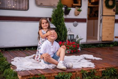 Kız kardeşi erkek kardeşinin gözlerini kapatıyor, arkasında dikiliyor, dikizcilik oynuyor, gülüyor. Küçük kız oğlanı yanağından öpüyor, karavanda sarılıyor, gezici evde. Yaz pikniği aile kamp konsepti