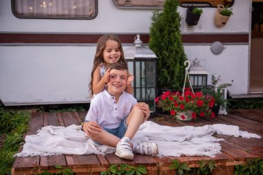 Kız kardeşi erkek kardeşinin gözlerini kapatıyor, arkasında dikiliyor, dikizcilik oynuyor, gülüyor. Küçük kız oğlanı yanağından öpüyor, karavanda sarılıyor, gezici evde. Yaz pikniği aile kamp konsepti