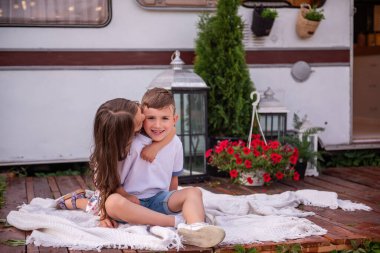 Kız kardeşi erkek kardeşinin gözlerini kapatıyor, arkasında dikiliyor, dikizcilik oynuyor, gülüyor. Küçük kız oğlanı yanağından öpüyor, karavanda sarılıyor, gezici evde. Yaz pikniği aile kamp konsepti