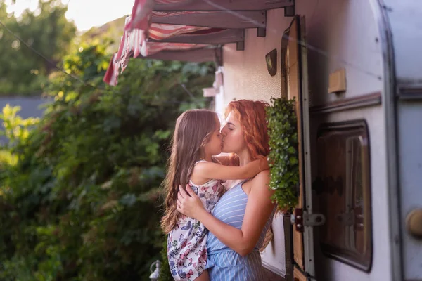 Güzel, kızıl saçlı genç bir anne, küçük kızını nazikçe kucağında tutuyor ve karavan kamyonuyla evinin yakınında kucağına alıyor. Kızlar gülümsüyor. Neşeli, özenli, mutlu annelik. Çocuklarla aile seyahati hafta sonu
