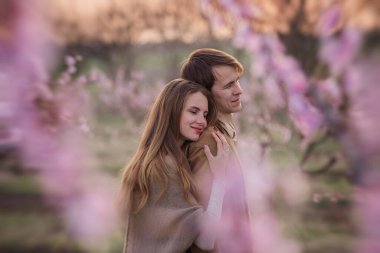 Gün batımında çiçek açan şeftali gül bahçelerinde aşık mutlu bir çift. Genç kadın erkeğin arkasında duruyor, sarılıyor, şefkatle ve tutkuyla öpüyor. Romantik bir randevu, sevgililer balayı hafta sonu şehir dışında.
