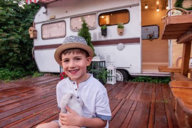 Hasır şapkalı küçük bir çocuğun portresi elinde tüylü bir tavşanla evdeki bir karavan kamyonunun yanında oturuyor. Gülüşmeler, evcil tavşanla oynamalar, piknik kampında evcil hayvanlarla gezmeler.