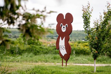 Magdachest, Moldova, 06-06-2021. Yolun kenarında yeşil çimlerin üzerinde olimpiyat yüzüklü bir olimpiyat ayısının retro figürü duruyor.. 