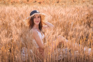 Buğday ve çavdar dikenli altın bir tarlada hasır şapkalı genç sarışın kadın. Kahverengi gözlü güzel bir kızın yakın plan portresi. Hafta sonu şehir dışında yürüyüş. Tarım dokusu