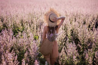 Hasır şapkalı genç sarışın kadın çiçek açan pembe adaçayının arka planına bakıyor. Elinde çiçek tutan güzel bir kızın yakın plan portresi. Tarım dokusu