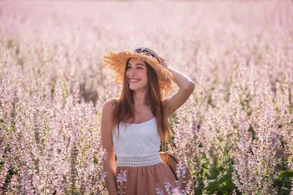 ピンクのセージの開花フィールドの背景にシフォンパウダージャンプスーツの若いブロンドの女性 藁帽子をかぶった美しい少女の肖像画 週末は街の外を歩く 農業の食感 — ストック写真