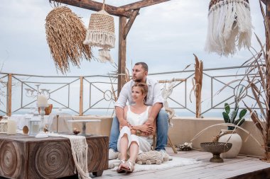 Beyaz elbiseli mutlu orta yaşlı çift, çatıda, denize bakan terasta oturuyor. Aile evlilik yıldönümünü kutluyor. İç mekan Maracans, Hindistan, eko tarzı