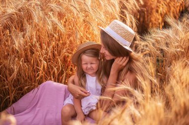 Anne ve kızının buğday tarlasında çiğ taneli saman şapkalı portresi. Genç kadın kızla eğleniyor, birbirlerini çavdar viskisi ile gıdıklıyor, gülüyor ve sarılıyorlar. Kırsal