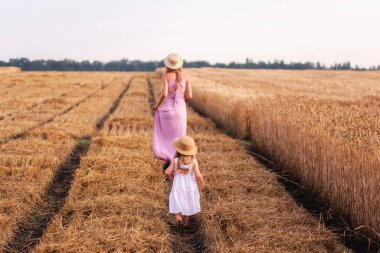 Kızı annenin elini tutar, gün batımında altın buğday tarlası boyunca yürür. Genç bir kadın ve pembe elbiseli bir kız ve hasır şapkalı bir kız çavdar ekmeğinin arasında, ayakları çamurun içinde duruyorlar. Kırsalda yürüyen bir zenci.