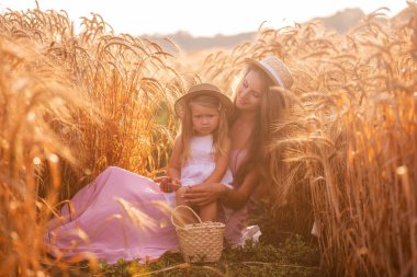 Anne ve kızının buğday tarlasında çiğ taneli saman şapkalı portresi. Genç kadın kızla eğleniyor, birbirlerini çavdar viskisi ile gıdıklıyor, gülüyor ve sarılıyorlar. Kırsal