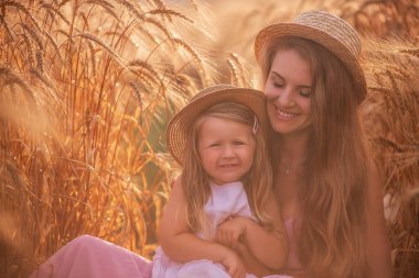 Anne ve kızının buğday tarlasında çiğ taneli saman şapkalı portresi. Genç kadın kızla eğleniyor, birbirlerini çavdar viskisi ile gıdıklıyor, gülüyor ve sarılıyorlar. Kırsal