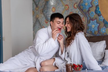 Genç adam yatakta güzel bir kadına çikolata kaplı çilek yediriyor. Beyaz önlüklü âşıklar eğleniyor, gülüyor, alay ediyor, çilekleri mermer tepside çikolata ezmesine batırıyorlar.