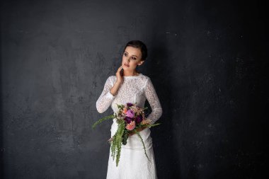 Duvağı olmayan beyaz bir elbise içindeki moda gelini, yeşil eğreltiotu ve burgundy kasımpatı buketinden oluşan orijinal bir düğün buketi tutuyor. Siyah dokuya yakın gülümseyen genç bir kadın. Boşluğu kopyala