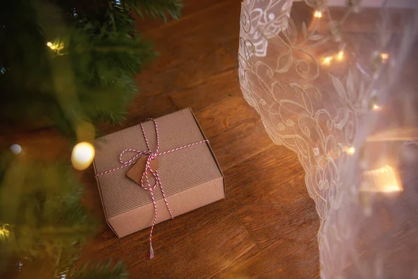 在绿色圣诞树的枝下 挂着手工包装的新年礼物 上面绑着一根白红的线 上面附有实现愿望的卡片 木制背景明亮的花环与玩具 复制空间 — 图库照片
