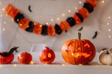 Cadılar Bayramı için zencefilli ve siyah tonlu tebrik kartı. Turuncu balkabakları beyaz bir masada yatar. Örümcek ağları ve siyah yarasaların olduğu kağıt bir çelenk ise arka planda asılı durur. Uzayı kopyala Şenlikli iç mekan