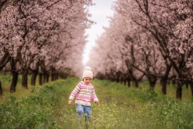 Yürüyen çocuk canlı bir bahar bahçesini keşfediyor, çimenli bir yolda yürüyor çiçek açan pembe badem ağaçlarıyla sıralanmış, yeni hayatı ve doğadaki çocukluğun masumiyetini kutluyor.
