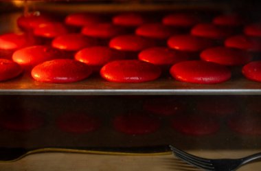 Sıcak bir fırında fırın tepsisinde yükselen kırmızı badem kurabiyeleri ev yapımı pişirme sırasında hassas, havadar Fransız hamur işlerine dönüşürken ısı altında kabaran canlı kırmızı kabuklar.