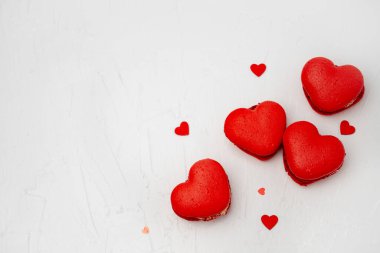 Dört kırmızı kalp şeklinde badem kurabiyesi ve küçük konfeti kalbi basit, beyaz bir arka planda dizilmiş aşk kutlaması için tatlı ve romantik bir ortam yaratıyor.