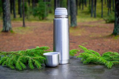 Yanında açık bir kapağı olan termos. Köknar dalları olan ahşap bir yüzey üzerinde. Arka planda doğa. Soğuk mevsimde açık hava eğlencesi kavramı..