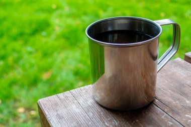 Kamp yaparken seyahat fincanının yakın çekimi. Çay ya da ahşap masada kahve olan metal bardak. Boşluğu kopyala.