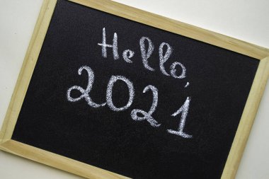 Ahşap çerçeveli siyah karatahta. Tebeşir el yazısıyla yazılmış. Merhaba 2021. Beyaz arkaplanda.