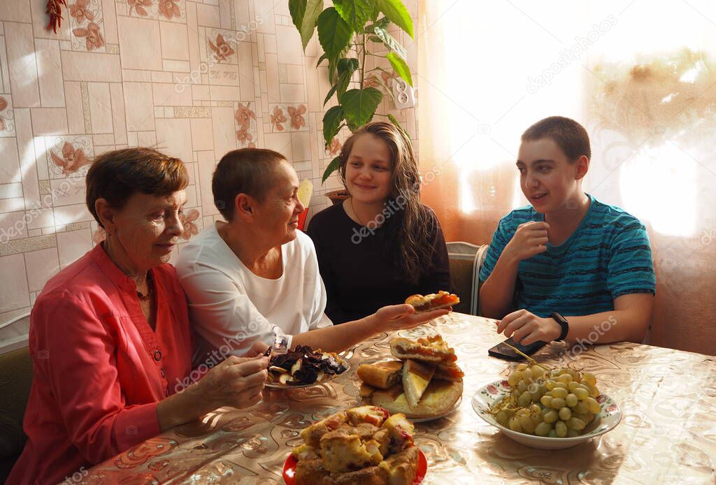 An elderly woman in bright clothes sets the table, arranges homemade cakes, prepares to welcome guests.Guests talk at the table, elderly people talk to young people, offer pies.