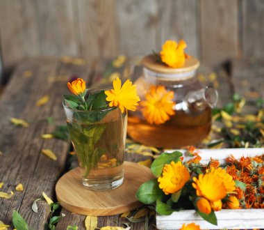 Medicinal autumn background.Herbal healthy marigold tea with a teapot, dried and fresh flowers on an autumn wooden background. clipart