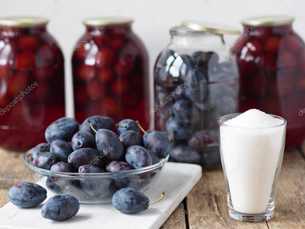 The idea of preserving plum compote for future use in glass jars on a wooden table. Blue plum on the background of ready-made compote in jars.