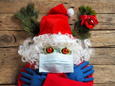 Tıbbi maske, eldiven ve tahta arka planda gözlük takmış korkmuş bir Noel Baba 'nın komik görüntüsü. Noel zamanı Covid 19 'u yakalamamak için koruyucu giysi kullanın. Kendine ve sevdiklerine iyi bak..